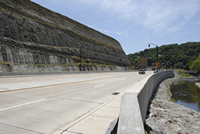 Photo of the new pavement cross-section with a high rock cut slope on the left and the new retaining wall on the right.