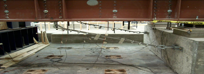Restrainer cables attached to steel beams and concrete substructure. Model is in laboratory and instrumented for testing.