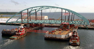 This is a photo showing the transport of the prefabricated Providence River Bridge. The photo shows the bridge being moved from land to two large ocean barges using SPMT's.