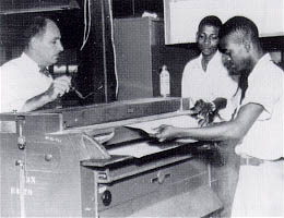Photo: J. Clarke Williams (left) observes Liberians operating Ozalid reproduction equipment.