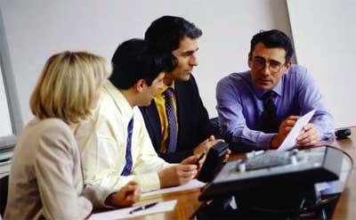 Photo: A woman and three men gathered around a meeting table, reviewing a paper