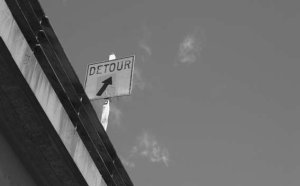 Cameo: A Detour sign situated on a bridge is captured from below with the sky as its backdrop.