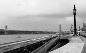 Cameo: A suspension bridge spans a river running perpendicular to an elevated highway, a railroad, and the retaining wall of a riverfront roadway.