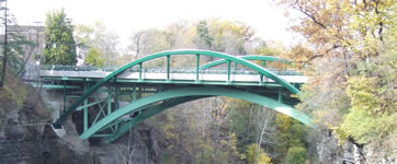 Photo showing the side view of the bridge, with the crest of the existing arch just underneath the bridge deck and the new tubular arches rising above the bridge deck.