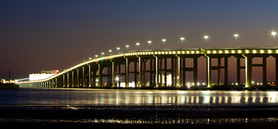 Photo showing the long, flowing curves to accommodate marine traffic under the Biloxi Bay Bridge, lighted against the night sky.