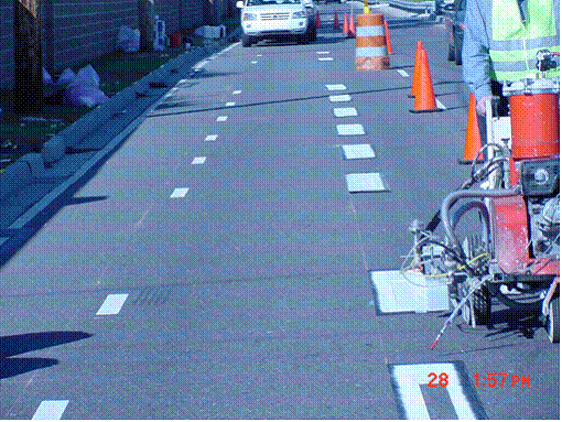 This picture shows the paint line application onto a mask placed on the road surface, which has a 3-foot by 4-inch slot in the middle.