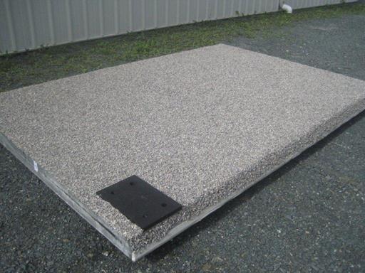 Figure 10. Photo. Adhesive and stone applied for course 1 of the wearing surface. Note the black prefabricated railing post pad and stone bonded to the sloped surface.