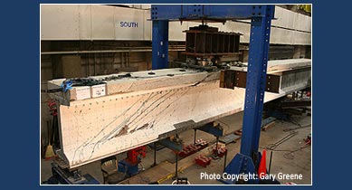 A picture showing shear testing of a 54-inch deep, LWHPC prestressed girder in the Structural Testing Laboratory at the Turner-Fairbank Highway Research Center. It displays cracking on the girder. (Photo Copyright: Gary Greene.)