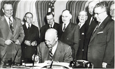 President Eisenhower signs the Federal-Aid Highway Act of 1954 on May 6, 1954. Watching are (left to right) Senator William F. Knowland (R-CA), Representative George A. Dondero (R-MI), Rep. Clifford Davis (D-TN), Senator Francis Case (SD), Rep. Homer D. Angell (R-OR), Senator Edward Martin (R-PA), and Rep. J. Harry McGregor (R-OH). On the fringe at far right is Rep. George H. Fallon (D-MD), who would play a key role in making the President's vision a reality in 1956. (Courtesy Dwight Eisenhower Library).