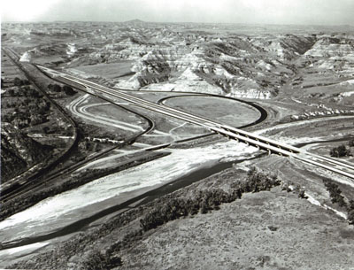 North Dakota - Looking westerly on Interstate 94 showing the West Medora Interchange nearing completion, the Little Missouri River Bridge, and present travel on U.S. highway 10.  The interchange shown will be the west terminus of Interstate 94 until the next portion west to the Montana State Line is completed.
