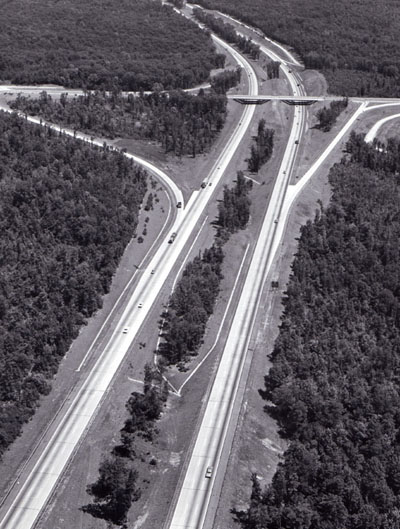 This section of Interstate highway (I-95 in Virginia) illustrates many of the safety features being built into the Interstate System, which will result in saving 8,000 lives each year when the system is complete.  These features include: controlled access, wide median dividing opposing traffic, long sight distances, gentle curvatures, all crossings separated by bridges or underpasses, wide paved shoulders, and acceleration and deceleration lanes.  Note also good design integrating esthetics and safety, including retention of trees in median and interchange area to reduce headlight glare, and adaptation of all highway elements to geographical features.