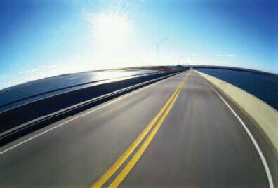 Page 16 Photograph: Wide-angle view looking forward from inside a car transiting a two-lane bridge with water on either side.