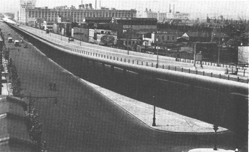 The Gowanus Elevated Parkway in New York, typical of elevated construction that may be employed near the centers of larger cities,cost $3,00,000 per mile. A large part of the cost was made up of the right-of-way expense engendered by widening of the street in which it was built. Even though attractively designed, elevated roadways are aesthetically undesirable in the midst of some parts of cities, such as residential areas. They also tend to divide a community and to act as barriers, at least psychologically, between the divided sections. This particular elevated structure in New York is appropriately located, however, because it divided a residential community (on the left) from an industrial and dock area.