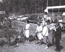 Along I-95 in Virginia, Federal Highway Administrator narrates as Lady Bird Johnson (left) shades her eyes after taking a turn with the shovel to fill in the hole around a dogwood tree planted for the occasion in cooperation with the Associated Clubs of Virginia for Roadside Development.  Muriel Humphrey, wife of Vice President Hubert H. Humphrey, is next to Whitton.  Third woman is unidentified.