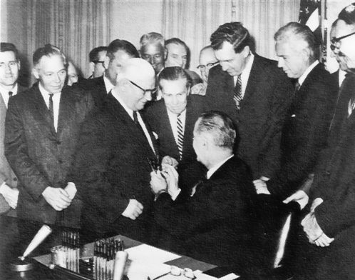 After signing the Federal-Aid Highway Act of 1964, President Lyndon B. Johnson hands one of the pens to Administrator Rex Whitton.