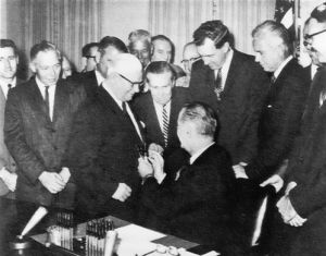 After signing the Federal-Aid Highway Act of 1964, President Lyndon B. Johnson hands one of the pens to Administrator Rex Whitton.