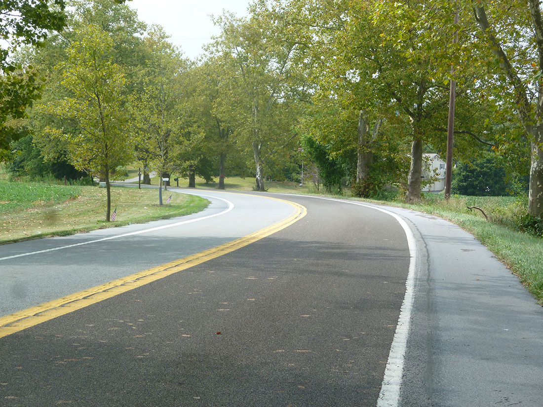 Photo of two-lane rural road curving right to left. On the rightmost lane, you can see a distinct difference in color and texture. This is HFST.
