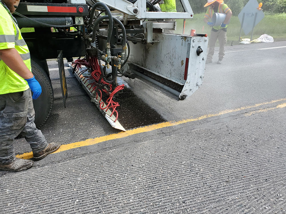 Close-up of the installation process, where a piece of equipment puts down high friction surface treatment on an existing roadway.