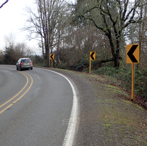 Photo of car on rural roadway curve with chevron signs and wide edge lines.