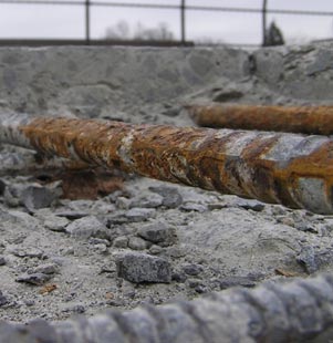 The first image, located in the lower-left corner of the slide, shows corrosion on two reinforcing bars of a concrete deck. The bars are exposed and there is a small pile of concrete rubble under the reinforcing bars.