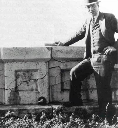 Figure A1.F1. Photo. Stanton Next to Wall with ASR. This photo is black and white showing Thomas Stanton standing next to a wall that is cracked as a result of ASR.