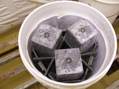Figure A3.F3. Photo. ASTM C 1293 Concrete Testing. This photo shows 3 concrete prisms placed vertically inside of a five gallon bucket. This is the typical storage set up for this test method.