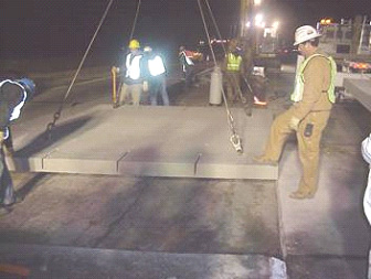 Precast panel installation in Colorado. A precast concrete panel is shown being lowered into position during nighttime construction. Three bar slots appear on the panel’s facing edge.