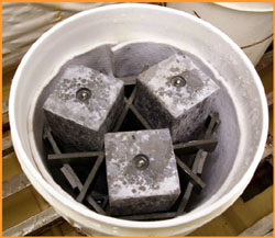 This image shows three rectangular shaped concrete samples in a five gallon plastic bucket. A cotton-like blanket has been placed inside the circumference of the bucket.