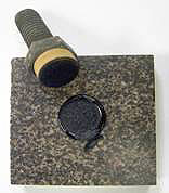 Figure 3. Photo. Pull-off test specimen on diabase stone after testing. The loading fixture and stone substrate are shown. The test sample was tested in the dry condition and failed cohesively within the mastic film as evident by the fact that mastic is observed on the ceramic surface of the loading fixture and on the diabase substrate. Figure 3. Photo. Pull-off test specimen on diabase stone after testing. The loading fixture and stone substrate are shown. The test sample was tested in the dry condition and failed cohesively within the mastic film as evident by the fact that mastic is observed on the ceramic surface of the loading fixture and on the diabase substrate.