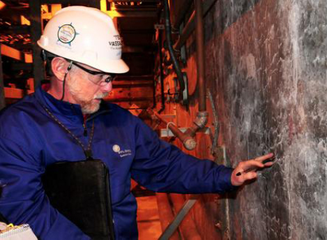 This image shows a man in a hard hat examining small cracks on the wall of an electric control tunnel.