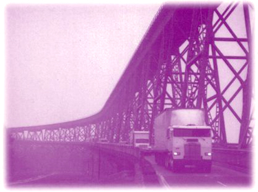 Cover picture of trucks and cars on a road that runs parallel to an elevated bridge.