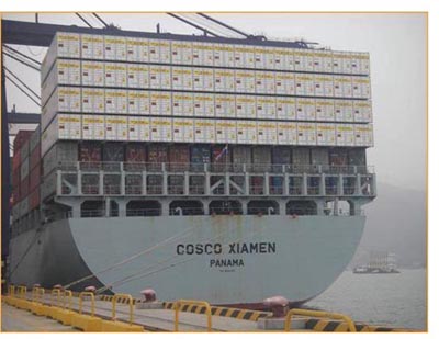 Photograph of a loaded container ship from the end, showing stacked container boxes six high.