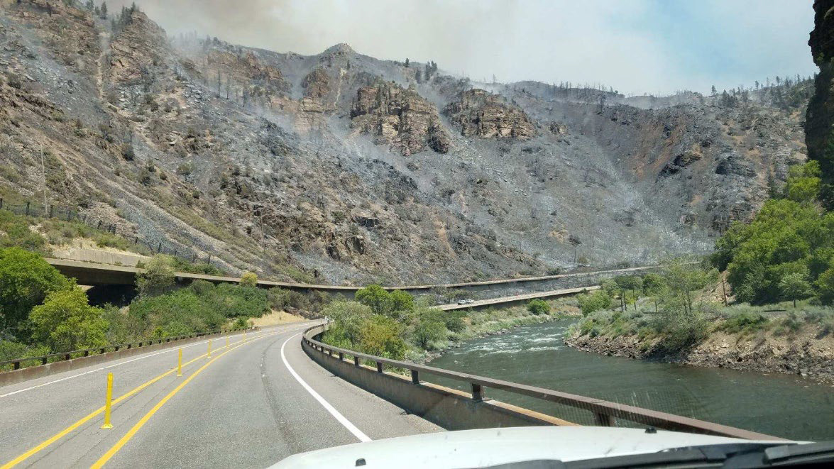 The Grizzly Creek fire left burn scars along I-70 in Glenwood Canyon. View from the windshield of a vehicle of the Rocky Mountains. The mountainside is charred and most of the vegetation is missing.