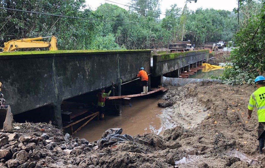 Side view of the historic WaipÄ� Bridge illustrating the damage caused by the historic rainfall event in April 2018. Bridge surrounded by mud flow and debris, as work crews attempt to repair damage.