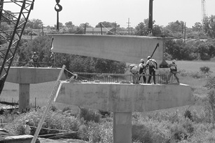 A concrete girder being guided into place between 2 pier caps