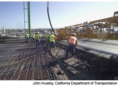 . Figure 4. Photo. I-580 concrete placement. Concrete is poured for the new I-580 connector ramp. Nine workers are visible.