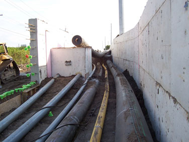 Figure 2. Photo. Links I Utility Corridor, Tampa, Florida. Six utility pipes lie next to each other horizontally in a partially built structure, with a wall on the right side and a partial wall on the left side.