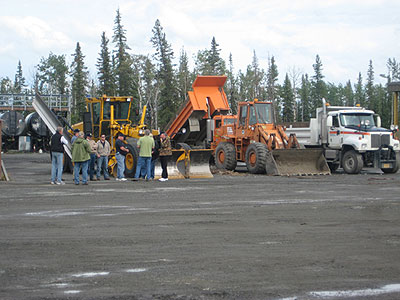 Eight participants in the Western Maintenance Scanning Tour visit the Tazlina Maintenance Station in Alaska's Northern Region. Three maintenance trucks are parked at the station.