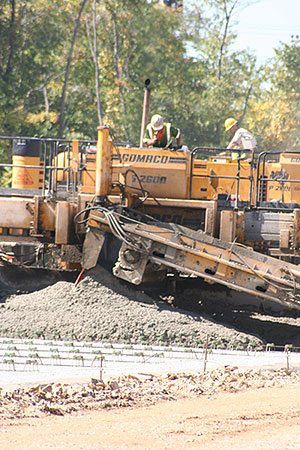 Concrete construction equipment. Two workers with hard hats are operating the equipment.