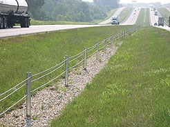 Cable median barrier in median between two 2-lane highways. Traffic is moving on the highways.