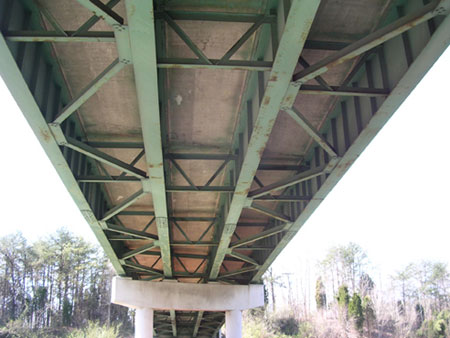 Photo. A view of typical connections, attachments, and details in steel bridges. The photo shows the underside of a steel bridge, including steel girders and attachments.