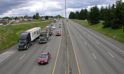 Figure 7. Photo. A view of a highway with three lanes in each direction. Trucks and cars are traveling on the highway.