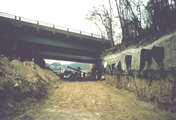 Figure 4. Photo. A soil nail wall is constructed to widen a roadway underneath an existing bridge near Olympia, WA. The soil nail wall is to the right of the existing bridge.