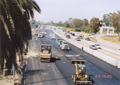 Figure 2. Photo. Two lanes of I-710 in Long Beach, CA, are closed for reconstruction. Trucks, pavers, and other pieces of road construction equipment are visible.