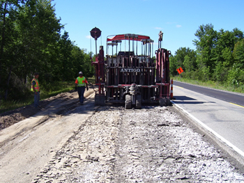 Figure 4. Photo. The asphalt pavement is rubblized on M-115 in Clare County, Michigan. Two roadway workers are visible.