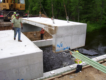 Figure 5. Photo. The mid-section of the precast concrete superstructure for a bridge on M-115 is placed. Three workers are visible.