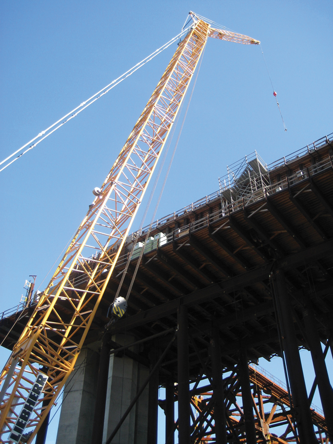 A ground-level view looking up at a crane towering over a bridge construction project.