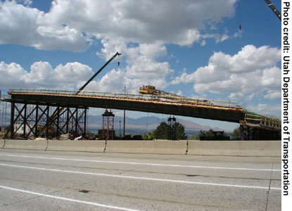 Figure 1. Photo. A view of the new 4500 South Bridge in Salt Lake City. The image shows the offsite construction of the bridge superstructure. A crane, other construction equipment, and scaffolding are visible.