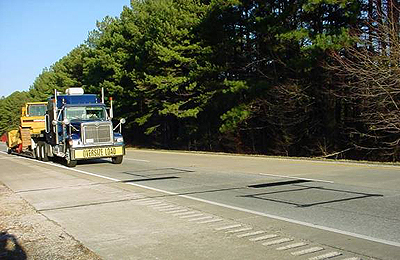  A view of a tractor-trailer truck approaching a weigh-in-motion installation in Arkansas. On the front of the truck is a banner that reads "Oversize Load."