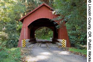 A view of the tree-lined approach to Oregon's Yachats Covered Bridge in Lincoln County. The wooden bridge is painted red.